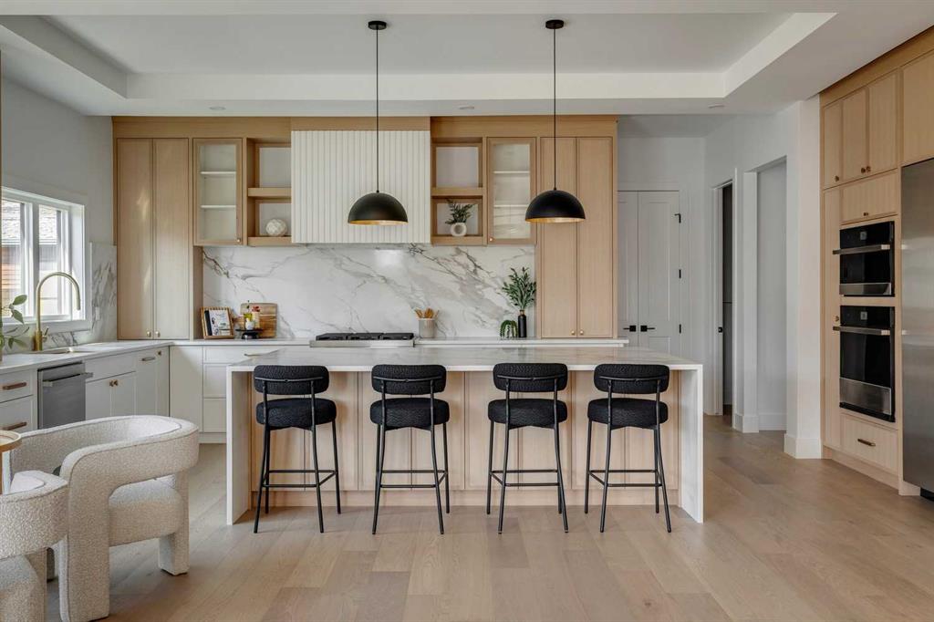 High-end kitchen showcasing Calgary custom home design with light wood coffered ceilings, white oak floors, and a luxury white waterfall island with black barstools.
