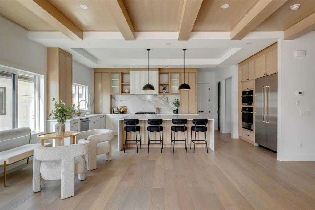 High-end kitchen showcasing Calgary custom home design with light wood coffered ceilings, white oak floors, and a luxury white waterfall island with black barstools.