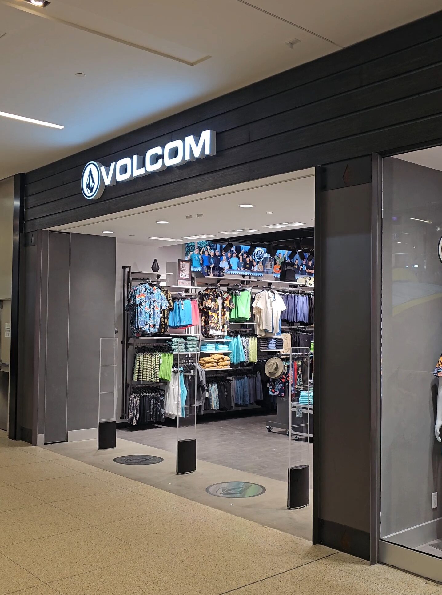 Volcom retail storefront at West Edmonton Mall featuring a modern illuminated logo, dark wood-paneled facade, and a wide-open entrance showing the interior layout and mannequin displays.