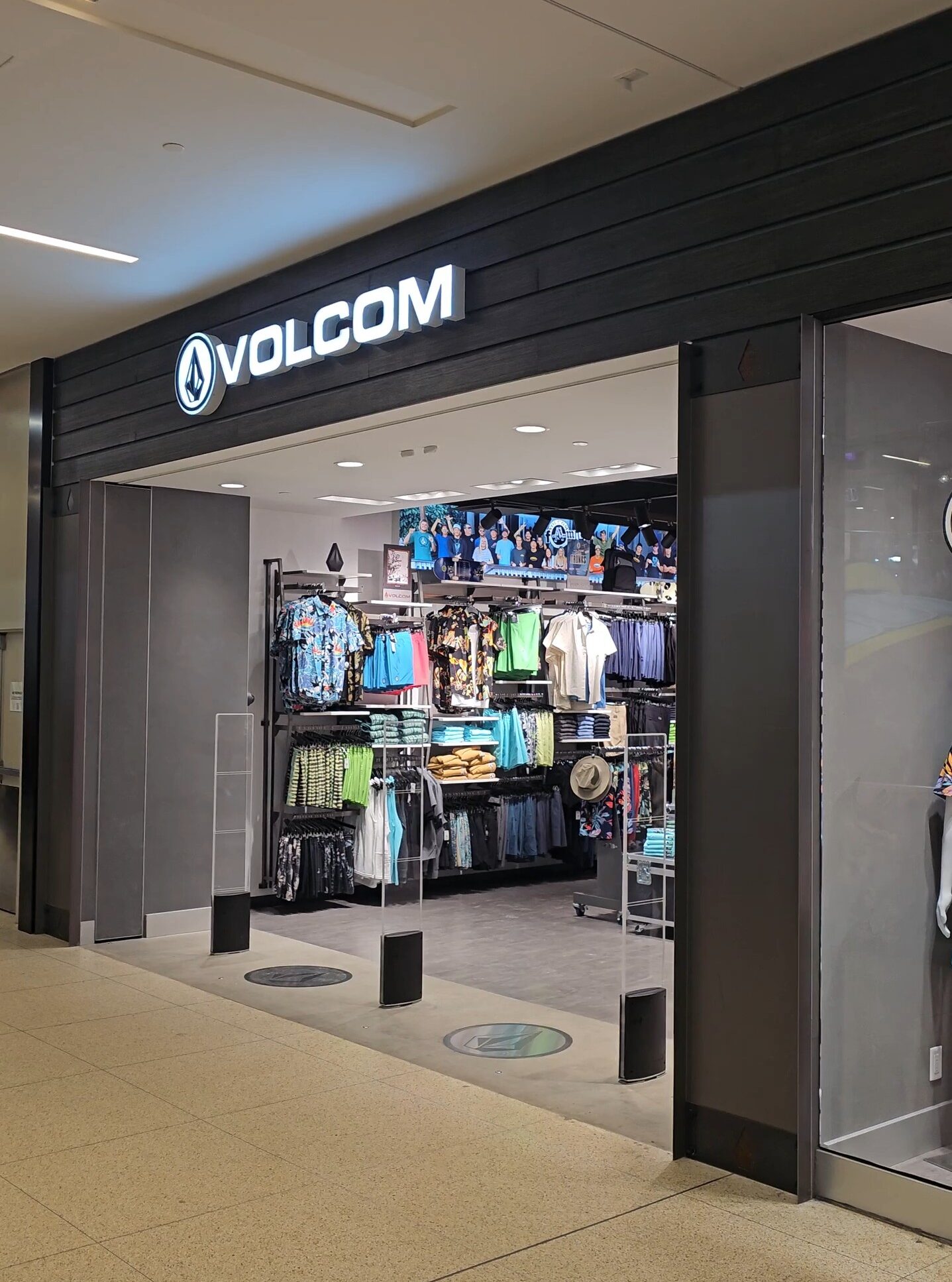 Volcom retail storefront at West Edmonton Mall featuring a modern illuminated logo, dark wood-paneled facade, and a wide-open entrance showing the interior layout and mannequin displays.